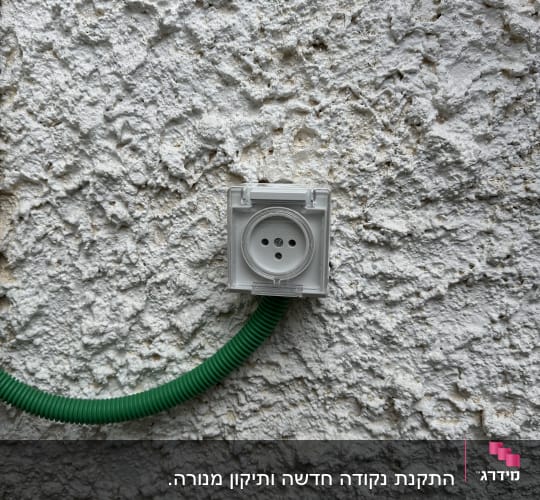 שקע חשמלי מותקן על קיר עם צינור ירוק